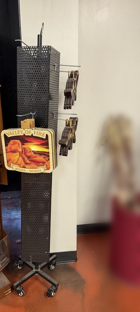 A black perforated spinner display stocked with Valley of Fire, Moapa, Nevada wood ornaments in a retail shop