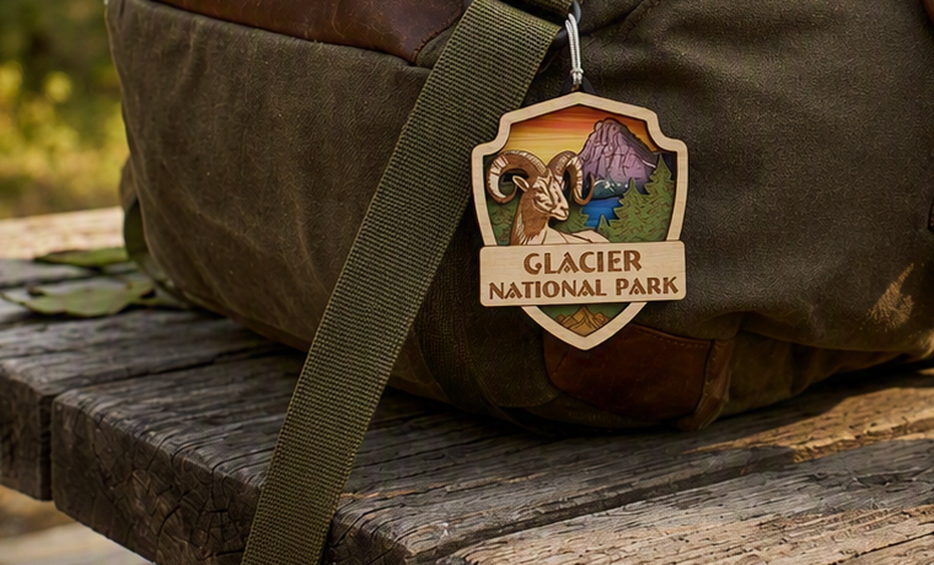 Custom laser-engraved wood badge ornament for Glacier National Park, featuring a bighorn sheep, hanging from a bag strap